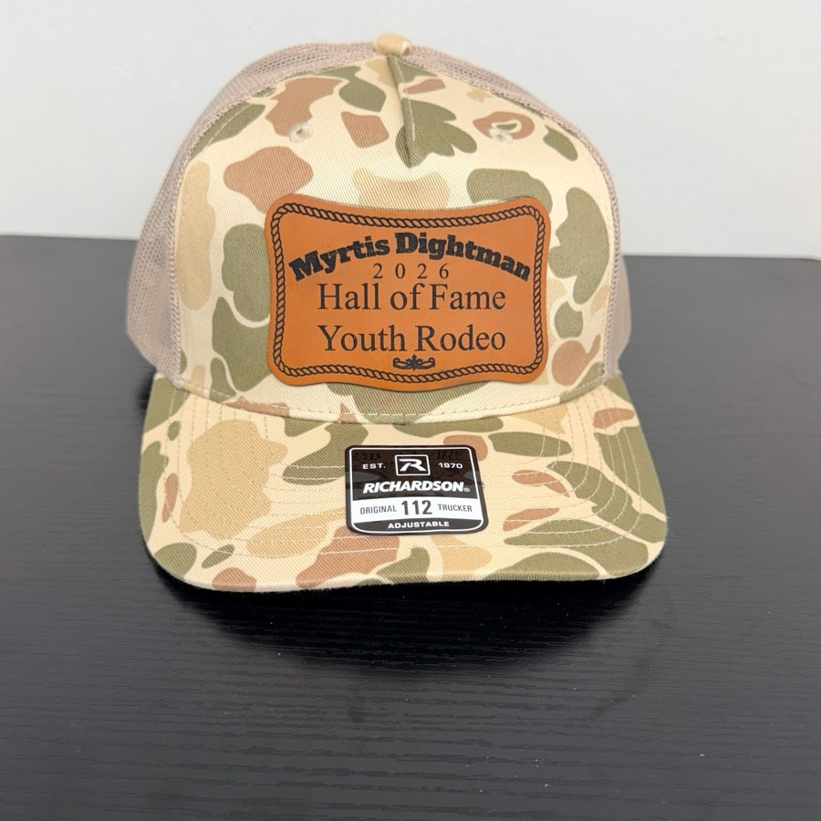 Myrtis Dightman cap in tan and olive camouflage with brown Hall of Fame Youth Rodeo patch, front view